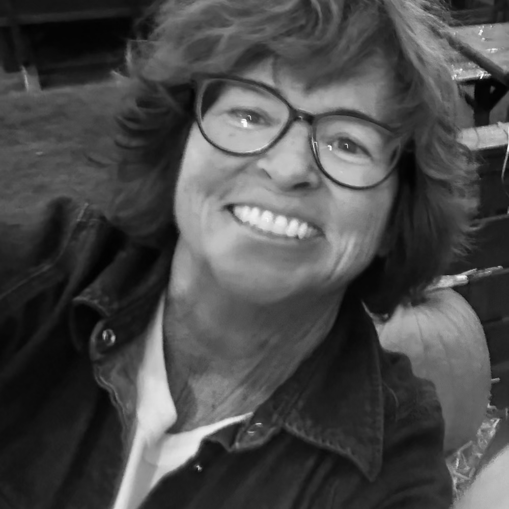 Black and white photo of a person with glasses smiling outdoors.