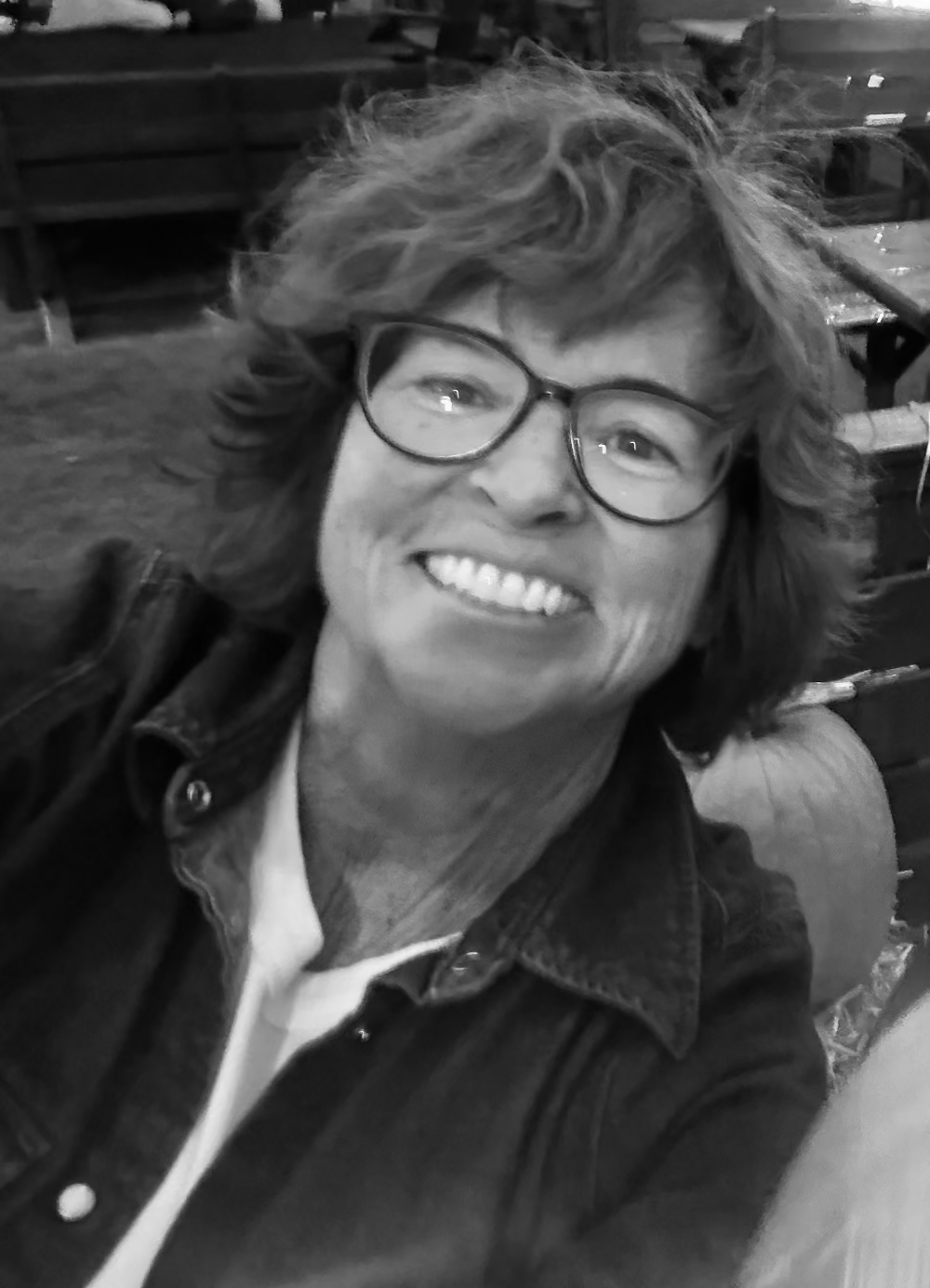 Black and white photo of a person with glasses smiling outdoors.